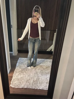 Vit kabelstickad kofta med knappar Gant - Säljer en vit kabelstickad kofta med knappar framtill. Koftan har långa ärmar och en klassisk rund halsringning. Perfekt att slänga över en topp för en chill och stilren look.