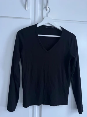 Svart v-ringad långärmad topp - En enkel och stilren svart topp med v-ringning och långa ärmar. Perfekt basplagg som funkar till allt. Tillverkad i mjuk bomull för skön känsla hela dagen.