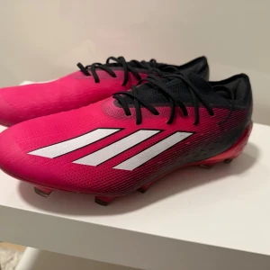 Rosa adidas fotbollsskor med snörning - Säljer ett par snygga rosa och svarta adidas fotbollsskor med klassiska vita ränder på sidan. Skorna har snörning och är tillverkade i syntetmaterial för bästa prestanda på planen. Perfekta för dig som vill sticka ut på matchen!