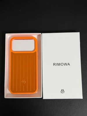 Orange 17 Pro Max mobilskal från Rimowa - Snyggt orange mobilskal från Rimowa med räfflad design och stor öppning för kameran. Skalet är tillverkat i tålig plast och har en modern, stilren look. Perfekt för dig som vill ha ett unikt och trendigt skydd till din mobil.