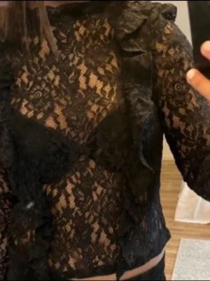 Svart spetsblus med volangdetaljer - Säljer en svart, långärmad blus i spets med volangdetaljer framtill