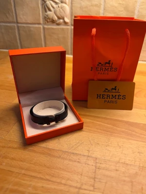 Herm4ès svart läderarmband - Snyggt svart armband från Herm4ès i äkta läder med elegant metallspänne. Kommer i original orange Herm4ès-förpackning och påse, perfekt för dig som gillar exklusiva accessoarer med stilren design.