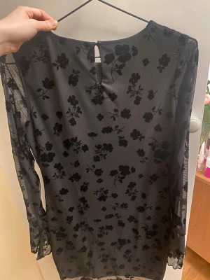 Svart festklänning  - Snygg svart kortklänning från Gina Tricot med transparenta meshärmar och sammetsliknande blommigt mönster. Klänningen har rund halsringning och knapp i nacken. Perfekt för dig som vill ha en trendig och elegant outfit!!💕💕