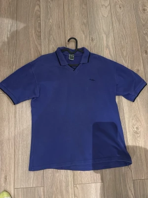 Blå sport pikétröja från Björn Borg  - Klassisk blå pikétröja från Björn Borg med krage och korta ärmar. Tröjan har en liten broderad logga på bröstet och är tillverkad i bomull. Perfekt för en avslappnad och stilren look. Storlek är M men passar mer som en L