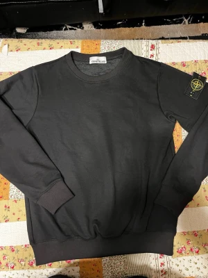 Stone Island tröja  - Svart sweatshirt från Stone Island med klassisk rund hals och ribbade muddar. Tröjan har den ikoniska Stone Island-loggan på vänster ärm. Tillverkad i mjuk bomull för en skön och avslappnad stil. Helt ny 