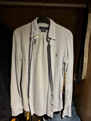 Ralph Lauren skjorta - Snygg blå- och vitrandig skjorta från Ralph Lauren i slim fit. Inga defekter eller liknande, använt några gånger och håller ett väldigt bra skick. Storlek S!