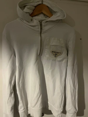 Vit hoodie från Prada med half zip - Snygg Prada tröja med unik designe. Säljer den för 1800kr nytt pris är 6000kr (ni får utgå skick från fotorna) ( står inte för retur om den inte passar) dom enda defekterna är att den har tappat färg vid smörerna (obs inga snören) 