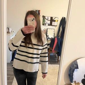 Beige stickad tröja med svarta ränder - Trendig beige stickad tröja med svarta horisontella ränder och rund hals. Tröjan har en avslappnad passform och ribbade muddar vid ärmslut och nederkant. Perfekt för en stilren och avslappnad look.