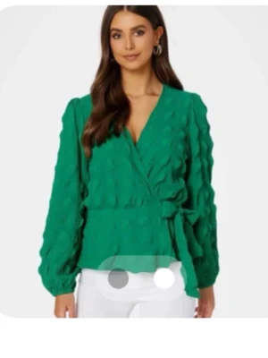 Grön omlottblus med knytband - Stilren grön omlottblus med knytband i midjan och strukturmönster. Blusen har långa ärmar med lätt puff och v-ringad hals. Använd 1 gång 💕