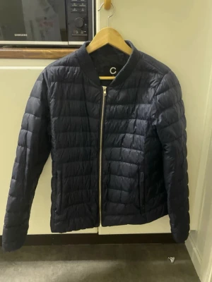 Mörkblå dunjacka från Cubus  - Snygg mörkblå dunjacka från Cubus med quiltad design och dragkedja framtill. Jackan har en klassisk passform och är perfekt för mest höstliga och kyliga dagar. Enkel och stilren look som passar till många outfits.