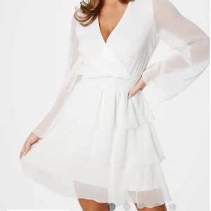 Vit omlottklänning med volanger - Superfin vit kortklänning med omlottliv, v-ringning och långa transparenta ärmar. Perfekt för sommarens alla tillfällen! Materialet känns lätt och luftigt. Köpt från bubbleroom för 699kr