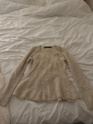 Beige ribbstickad tröja  - Beige ribbstickad tröja från Vero Moda med utsvängd passform och rund halsringning. Långa ärmar och mjukt material som känns skönt mot huden. Perfekt att styla med jeans eller kjol för en avslappnad look.