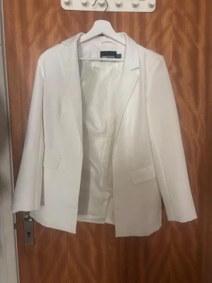 Vit kavaj från Pieces - Stilren vit kavaj från Pieces med klassisk krage och två fickor framtill. Kavajen har en rak passform och är helfodrad för extra komfort. Perfekt att styla till olika looks och ger en fräsch vibe till outfiten. Super fin och är i ett bra skick
