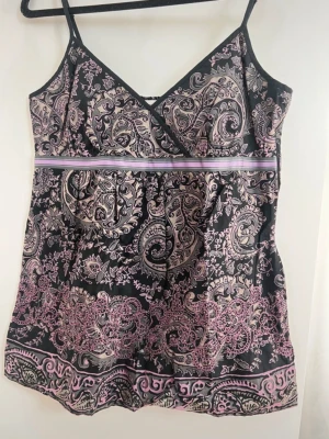 Linne Esprit - Säljer ett svart linne med tunna axelband och paisleymönster i lila och beige. Toppen har dekorativa pärlor längs nederkanten och ett omlottliknande bröstparti. Jätte fint linne som är oanvänd. Lappen hänger kvar med extra pärlor vid behov. Justerbara band och dragkedja på sidan. Passar även för storleken M.