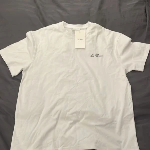 Vit t-shirt från Les Deux oversized - Snygg vit t-shirt från Les Deux med diskret svart broderad logga på bröstet. Klassisk passform och rund halsringning. Perfekt basplagg till garderoben och enkel att matcha med allt. Tillverkad i mjuk bomull för skön känsla.