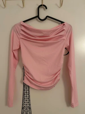 Ljusrosa långärmad topp med rynk från SHEIN  - Ljusrosa topp med långa ärmar och snygga rynkdetaljer vid halsringningen från SHEIN i storlek XS. Toppen har en offshoulder-design och är tillverkad i ett mjukt, stretchigt material som sitter bekvämt på kroppen. Aldrig använd men har inte prislappen kvar. 