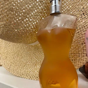 Jean Paul Gaultier Classique parfym - Ikonisk parfymflaska från Jean Paul Gaultier i form av en kvinnlig torso. Flaskan är genomskinlig med en varm bärnstensfärgad vätska och har en silverfärgad spraykork. Perfekt för dig som gillar unika och snygga parfymflaskor.