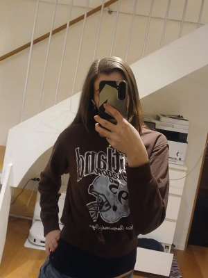 Brun hoodie med tryck  - Cool brun hoodie med stort vitt tryck och amerikansk fotbollshjälm på framsidan. Oversized passform och mjukt material, perfekt för en avslappnad streetstyle-look.