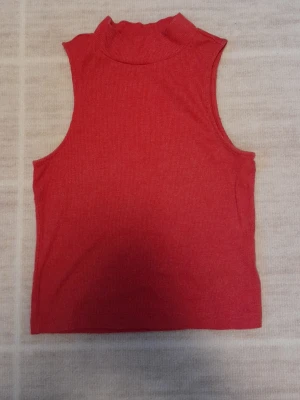Röd ribbad polotopp - Säljer en röd ribbad polotopp från H&M DIVIDED i storlek XS. Toppen är ärmlös med hög krage och har en tight passform. Perfekt att styla med jeans eller kjol för en enkel men snygg look. !!endast swish +frakt!!