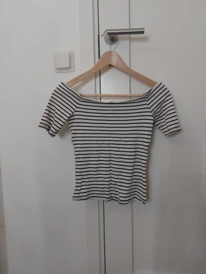 Randig offshoulder topp från H&M - Säljer en vit och svart randig offshoulder topp från H&M i storlek XS. Toppen har korta ärmar och en tight passform som framhäver axlarna. Aldrig använt ❣️