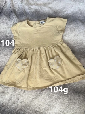 Gul tunika med hjärtfickor - Supersöt gul tunika från Polarn o pyreti. Tunikan har korta ärmar och två hjärtformade fickor framtill med vita prickar. Perfekt för dig som gillar gulliga detaljer och enkel stil.🌸 Fint använt skick. Storlek 104