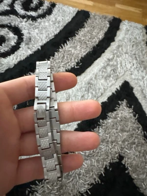 Lacoste armband herr - Bilderna visar ett metallarmband, troligen till en klocka, och ingen väst finns med. Ladda gärna upp bilder på västen om du vill ha hjälp att beskriva den.