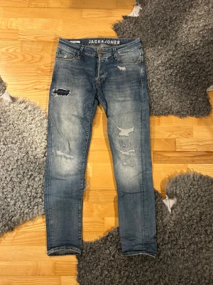 Blå slitna jeans från Jack & Jones - Säljer ett par blå jeans från Jack & Jones med slitna detaljer och hål på benen. Modellen har fem fickor, normal passform. Storlek 31/32.               Fråga gärna om fler bilder, mått mm! 🤝🏻✌🏼