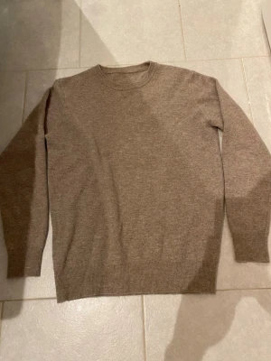 Beige stickad tröja i merino ull  - En enkel och stilren beige stickad tröja med rund halsringning och långa ärmar. Perfekt för lager på lager och funkar till allt. Mjuk och skön känsla tack vare ullblandningen. Ribbstickade muddar vid ärmslut och nederkant.