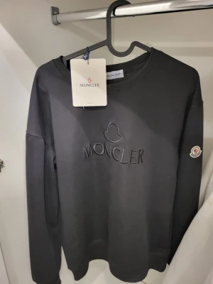 Svart sweatshirt från Moncler - Säljer en svart sweatshirt från Moncler med broderad logga på bröstet och Moncler-märke på ärmen. Tröjan har rund halsringning och långa ärmar. Perfekt för dig som gillar stilrena och exklusiva plagg.