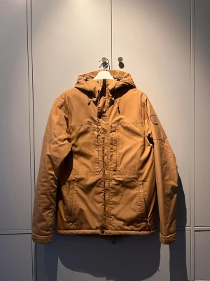 Fjällräven skogsö padded - Säljer en beige skogsö från Fjällräven med justerbar huva och dragkedja framtill. Jackan har två stora fickor, diskret logga på ärmen och quiltat foder i grått. Köpt cirka två år sedan men använd sparsamt en säsong.
