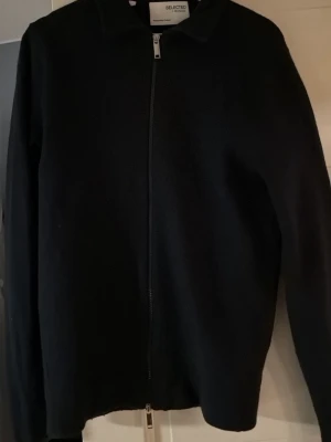 Marinblå ullkofta från Selected Homme - Säljer en stilren marinblå kofta från Selected Homme i mjuk ull. Koftan har hel dragkedja framtill, klassisk krage och lång ärm. Perfekt till lager på lager under höst och vinter. Enkel och clean look som funkar till det mesta.