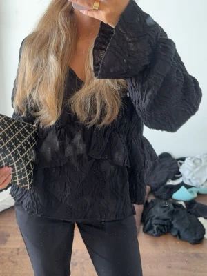 Svart volangblus med vida armar - Säljer denna otroligt fina svarta blusen med vida armar. Tyget har lite textur och passar super till både vardag och festligheter! 