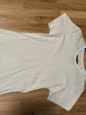 Vit t-shirt från Calvin Klein - Säljer en klassisk vit t-shirt från Calvin Klein i mjuk bomull. T-shirten har korta ärmar, rund halsringning och en diskret Calvin Klein-logga tryckt nertill. Perfekt basic-plagg med clean look och skön passform.