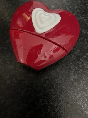 Escada hjärtformad parfymflaska - Snygg parfym från Escada i en unik röd hjärtformad flaska med vit detalj. Perfekt för dig som vill sticka ut med din doftaccessoar. Volym och ingredienser syns ej på bilderna.
