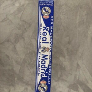 Real Madrid halsduk blåvit - Säljer en blåvit halsduk från Real Madrid med klubbens logga och texten 'Ser Madridista, un orgullo'. Perfekt för dig som vill visa ditt stöd på matchen eller i vardagen. Klassisk design med tydliga klubbfärger och emblem.