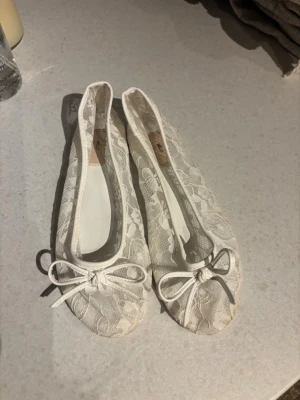 Vita spetsballerinaskor med rosett från Nelly - Säljer ett par vita ballerinaskor från Nelly med spetsdetaljer och söt rosett framtill. Skorna har rund tå och platt sula, perfekta till sommarens outfits. Materialet är spets över syntet och de är riktigt lätta på foten. Har använt de 1 gång på min konfamation. Smutsen under skorna går säkert och tvätta bort, de mesta del iallafall. Skriv om ni undrar något eller sådant