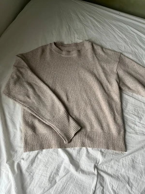 Beige stickad tröja med ribbade detaljer - Mysig beige stickad tröja med rund hals och breda ribbade muddar vid ärmslut och nederkant. Perfekt för lager på lager och chill dagar. Enkel och stilren design som passar till det mesta.