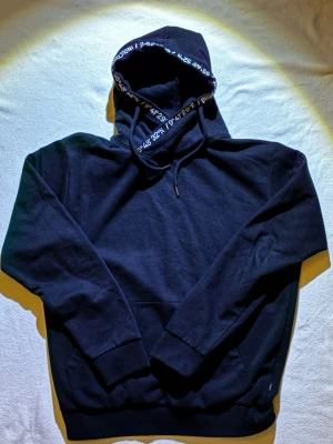 Svart hoodie med hög krage- bekväm - Snygg svart hoodie i mjukt och bekvämt material. Modellen har hög krage med snörning som ger en modern och unik look. Perfekt för vardag, skola eller chill outfits. Klassisk passform och lätt att matcha med allt. I fint skick.