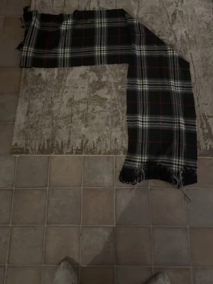 Svart rutig halsduk med fransar - En lång och mjuk halsduk i svart med klassiskt rutigt mönster i vitt och röda linjer. Halsduken har fransar i ändarna och passar perfekt för att ge din outfit en stilren touch. Perfekt accessoar för kyligare dagar.