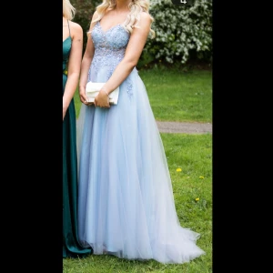 Ljusblå långklänning med pärlbroderi - Superfin ljusblå långklänning med tunna axelband och v-ringning. Överdelen är dekorerad med pärlbroderier och blommiga detaljer, medan kjolen är i flera lager av tunn tyll som ger en drömmig känsla. Perfekt till bal eller student! Använd på bal en gång så det finns lite skavanker från stranden och brunutan sol men inget som syns så och den har tagits hand om flitigt, ny pris 6000kr 