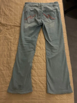 Ljusblå bootcut jeans från Nelly - Säljer ett par ljusblå bootcut jeans från Nelly med låg midja och snygga kontrastsömmar på bakfickorna. Jeansen har klassisk femficksdesign, vida ben och är tillverkade i mjukt denimtyg. Perfekta för dig som gillar retrovibbar och vill ha en avslappnad men trendig look.