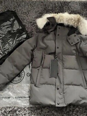 Grå dunjacka med pälskantad huva - Säljer en riktig grå dunjacka från Canada Goose med pälskantad huva och quiltad design. Jackan har dragkedja och knappar framtill samt flera praktiska fickor. Perfekt för kalla vinterdagar och riktigt snygg till alla outfits.