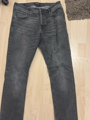 Grå slim jeans från Jack Jones  - Säljer ett par gråa slim fit jeans från Jack Jones Jeans i storlek 31/34. Jeansen har klassisk femficksdesign, knappgylf och diskreta slitningar för en cool look. Materialet är mjukt och stretchigt jeans för skön passform.
