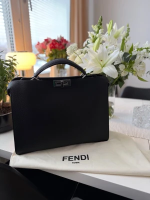 Fendi Peekaboo väska  - Säljer en stilren svart handväska/kontorsväska i modell Peekaboo från Fendi i exklusivt skinn. Insidan är fodrad i brunt läder och har smarta fack. Den kommer dessvärre inte längre till användning. Får lätt plats med en dator och böcker + dokument. Möts endast upp! Kan tänka mig gå ner i pris vid snabb affär!