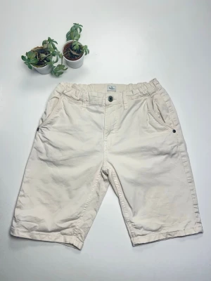 Beiga shorts från Pepe Jeans - Snygga beiga shorts från Pepe Jeans med elastisk midja och knappstängning. Klassisk passform med fickor fram och bak, samt diskret logga bak. Perfekta till sommaren och lätta att matcha med allt. 