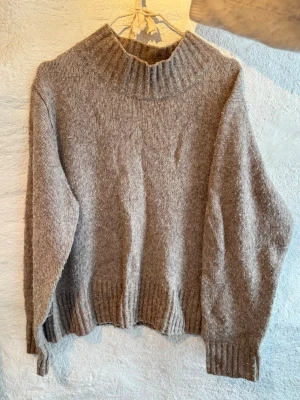 Beige stickad polotröja - Mysig beige stickad polotröja med bred ribbad krage och muddar. Tröjan har en relaxed passform och långa ärmar, perfekt för kyliga dagar. Passar storlek S-L