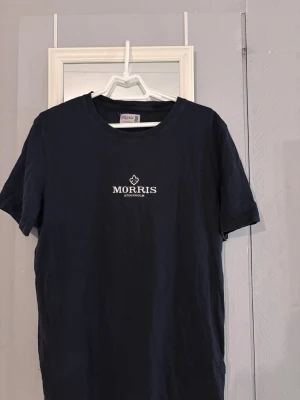 Svart t-shirt från Morris Stockholm XL - Snygg svart t-shirt från Morris Stockholm i storlek XL. Klassisk passform med rund hals och korta ärmar. Diskret Morris-logga broderad i vitt på bröstet. Tillverkad i mjuk bomull