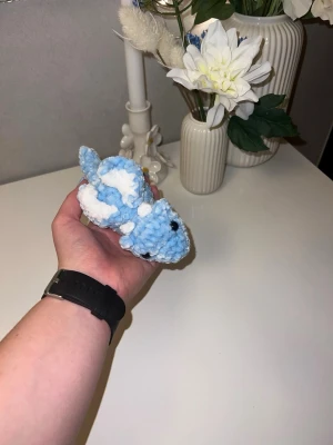 Ljusblå bäbisdrake med vita detaljer🩵🤍 - Denna urgulliga bäbisdrake vill hitta sitt nya hem🐉💚🩵🤍Den har hårda blåa ögon💙🤍 Den är ungefär likas stor som min handflata🐉 så cirka 15cm lång🩵 Vikrad med massa kärlek, med mjukt garn från Rusta🩵🤍
