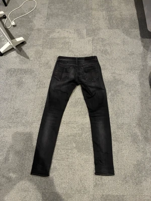 Svarta skinny jeans Tiger of Sweden - Säljer ett par svarta skinny jeans från Tiger of Sweden. Jeansen har klassisk femficksdesign, smal passform och är tillverkade i stretchigt jeanstyg. Snygga slitningar och diskret tvättad look ger dem en cool vibe.