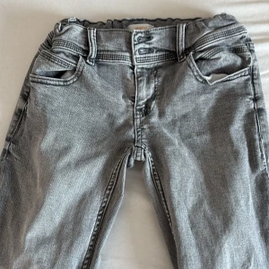 Grå jeans med stjärna från Gina Tricot - Säljer ett par grå jeans från Gina Tricot i storlek 158. Byxorna har raka ben, resår i midjan och en cool stjärndetalj på ena bakfickan. Klassisk femficksmodell i mjukt bomullsmaterial och snygg tvättad look.